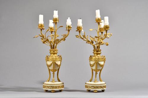 A pair of French Louis XVI style ormolu and white marble four branch candelabra, each urn issuing four foliate cast branches, with Bacchus cast masks