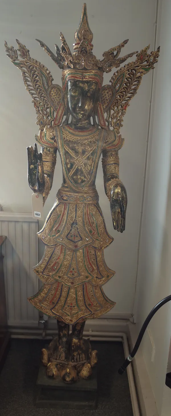 A Thai carved wood figure of a female temple god with crown and wings, gilt filigree against a black painted ground, 190cm high.
