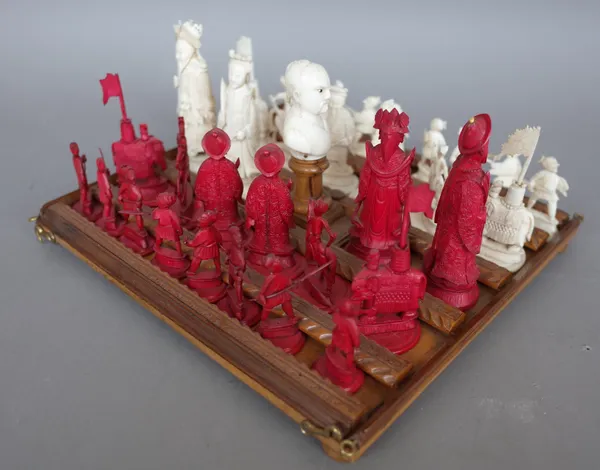 A Chinese stained ivory figural chess set, circa 1900, on a fitted and carved wooden plinth with perspex cover, King 10cm high.