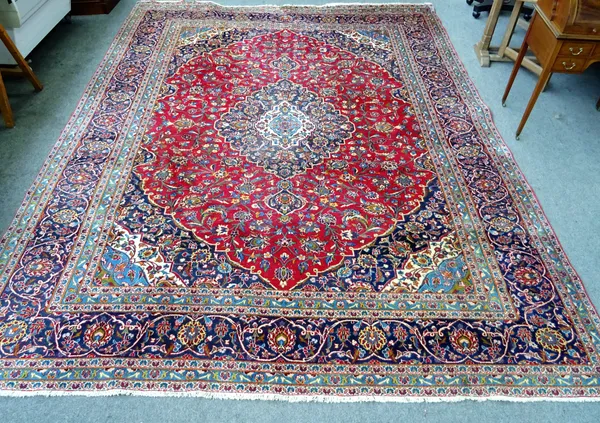 A large decorative Persian carpet in a variant of a Tabriz design, deep red field with polychrome floral decoration within deep blue spandrels, dark b