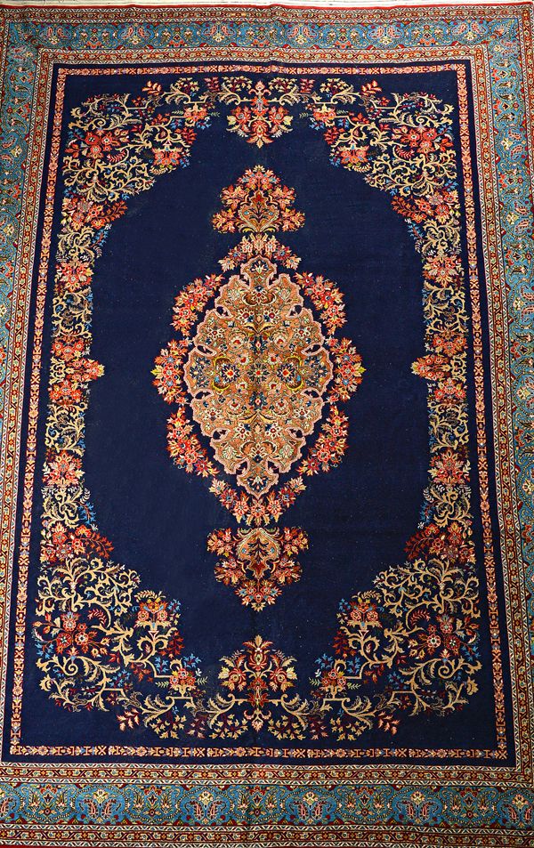 A part silk Kashan carpet, Persian, the plain dark indigo field with a delicate lobed brown medallion, a scrolling floral surround; a pale indigo bote