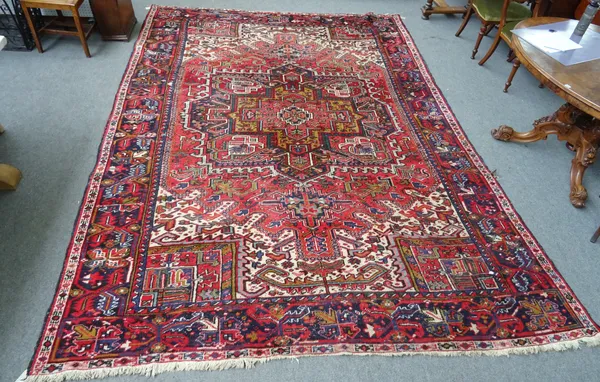 A Heriz carpet Persian, the madder field with a bold angular medallion, a black palmette and angular leaf border, 377cm x 273cm.