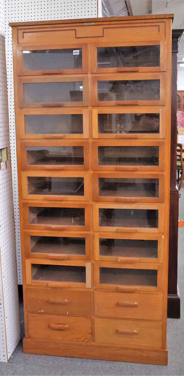 Dudley & Co Ltd; a mid-20th century oak haberdashery cabinet with two rows of eight glass fronted drawers over four solid drawers, 87cm wide x 194cm h