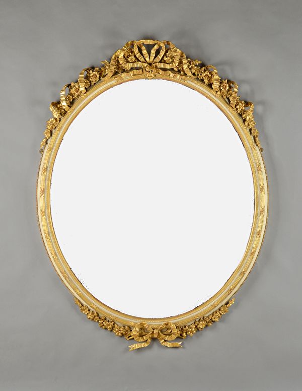 A large 19th century gilt and parcel cream painted oval wall mirror with ribbon tied floral crest and lower frieze, 109cm wide x 144cm high.  Illustra