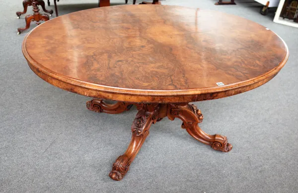 A Victorian oval figured walnut snap top loo table on four floral carved downswept supports, with retailer's plaque T H Filmer & Sons, Berners St, Oxf