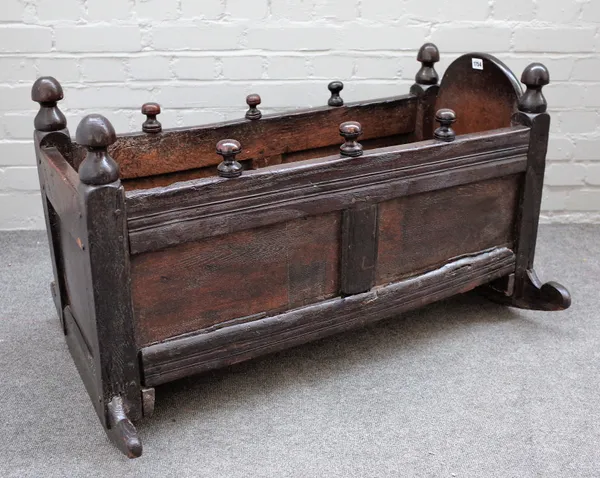 A 17th century oak rocking cradle with panelled sides and turned finials, 94cm wide x 57cm high.