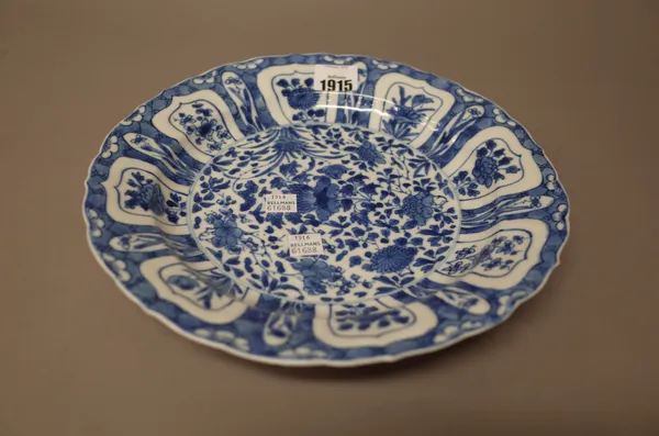 A Chinese blue and white plate, Kangxi, painted in the centre with flowers, beneath a panelled border enclosing flowers against a `cracked ice' ground