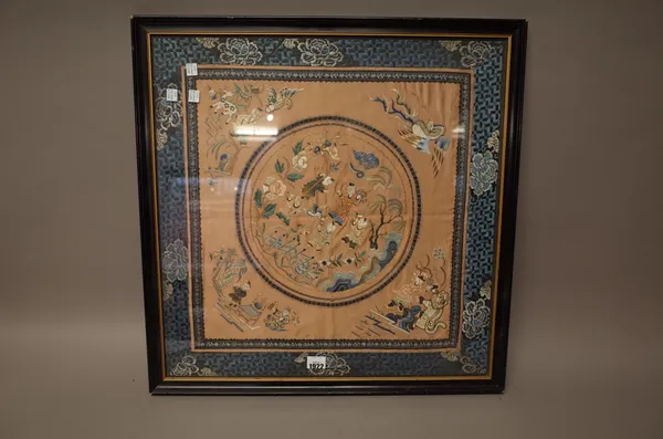 A Chinese embroidered panel, circa 1900, worked with a central circular medallion enclosing five boys in a landscape, framed in each corner with figur