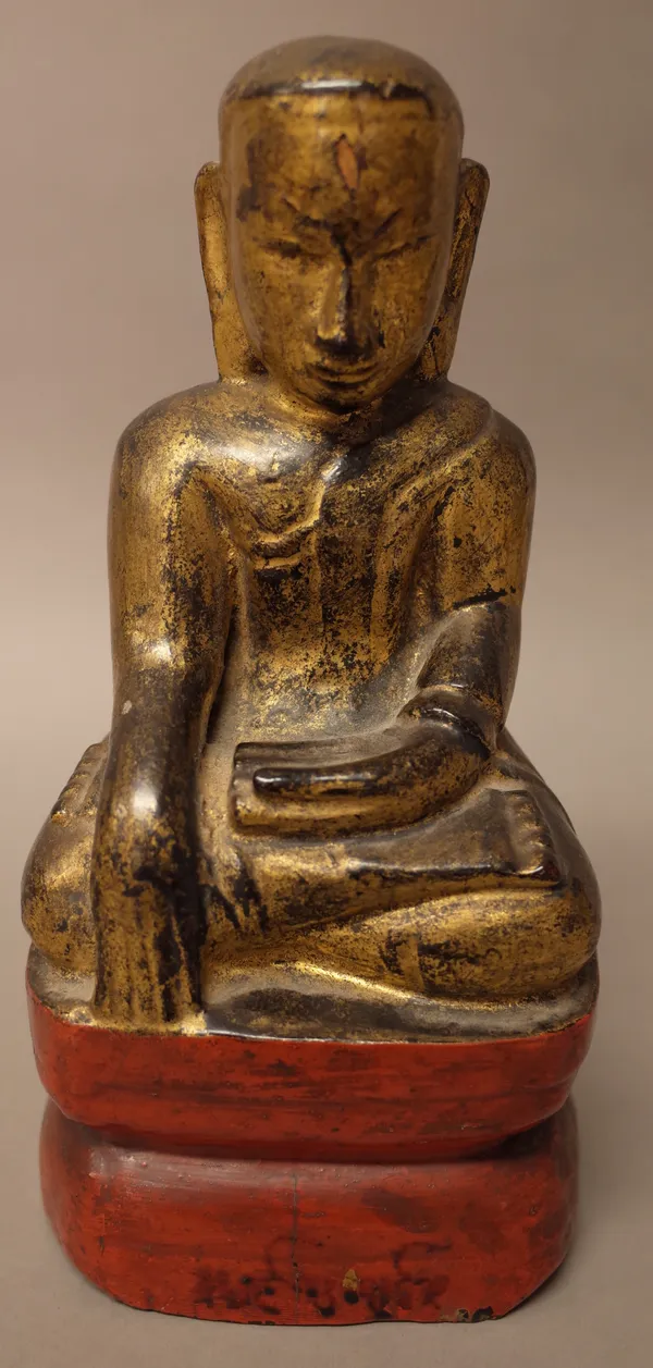 A giltwood and painted wood figure of a seated deity, possibly Tibetan, the base enclosing four scrolls, 24cm. high.