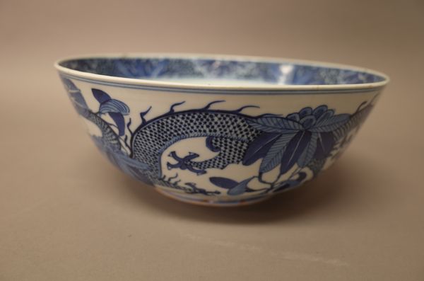 A Chinese blue and white bowl, late 19th century, painted in the interior with a panel of a dragon amongst flowers, the exterior painted with two drag