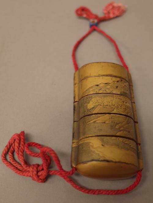 A Japanese gold lacquer four-case inro, Meiji period, decorated with  an extensive river landscape with a sailing vessel, bridge, buildings and mounta