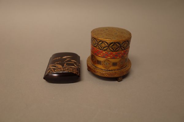 A small Japanese lacquer three-tired cylindrical box, cover and stand, Meiji period, decorated with geometric designs in various colours, the stand an