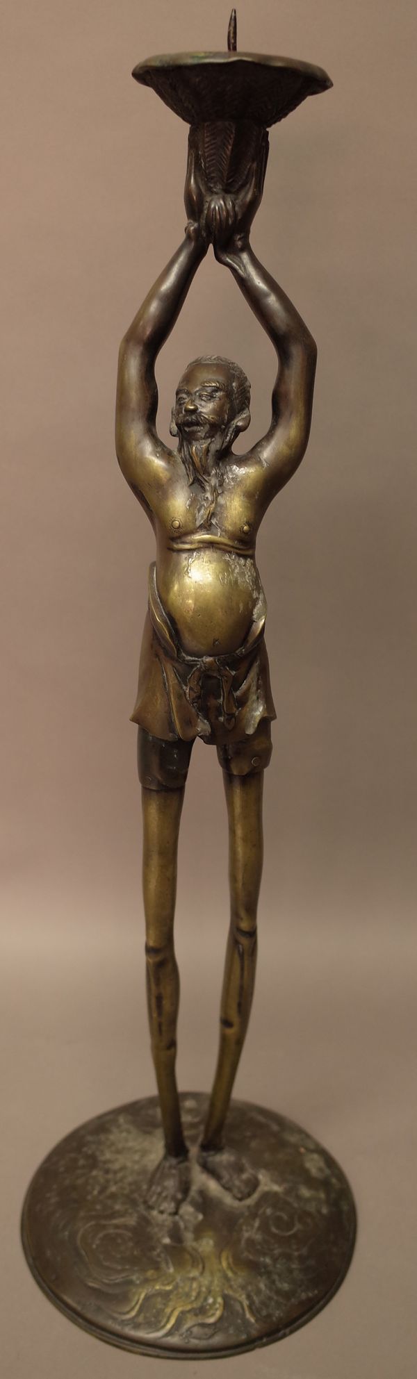 A tall Japanese bronze candlestick in the form of Ashinaga, the long-legged figure from Japanese folklore standing on a circular base with arms raised