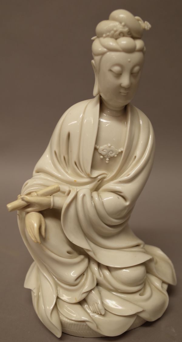 A Chinese blanc de chine figure of Guanyin, modelled seated holding a scroll in her left hand, the oval base with incised herringbone pattern, (a.f),