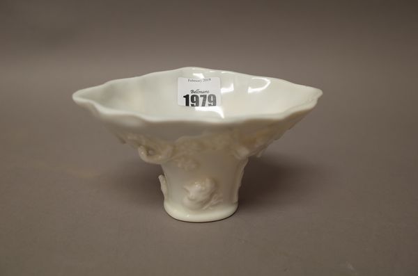 A Chinese blanc de chine libation cup. of rhinoceros-horn form, applied with dragons, deer, pine and prunus branches, 15.5cm. wide.