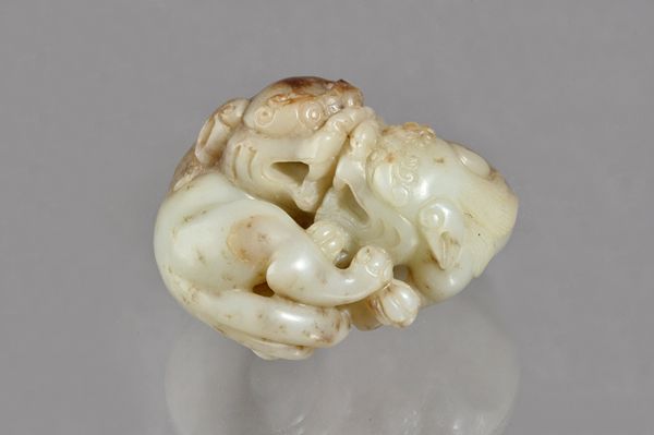 A Chinese brown and cream jade group of two Buddhist lions, possibly 17th century, carved in the round playfighting,6cm. wide. Illustrated