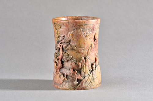 A Chinese soapstone brushpot, 18th/19th century, of slightly waisted cylindrical form, carved in deep relief with figures and a pavilion in a mountain