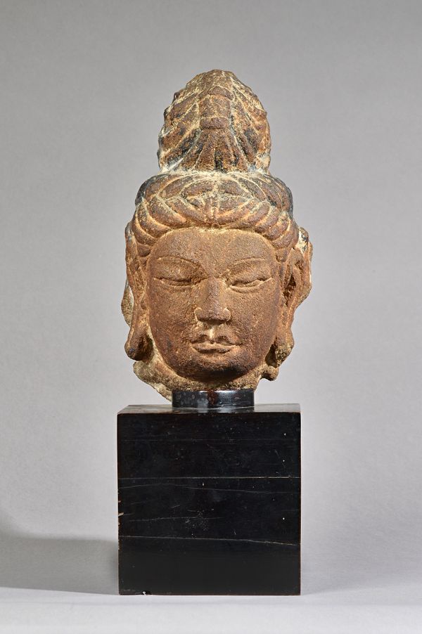 A Chinese carved stone head of Buddha, with downcast eyes in meditation, flanked by a large pair of pendulous earlobes, the hair tied in strands benea