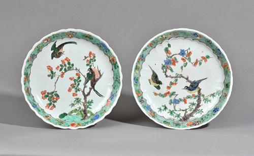 A pair of Chinese famille-verte plates, Kangxi, each painted with two birds amongst flowering branches, beneath a green `seeded' border enamelled with