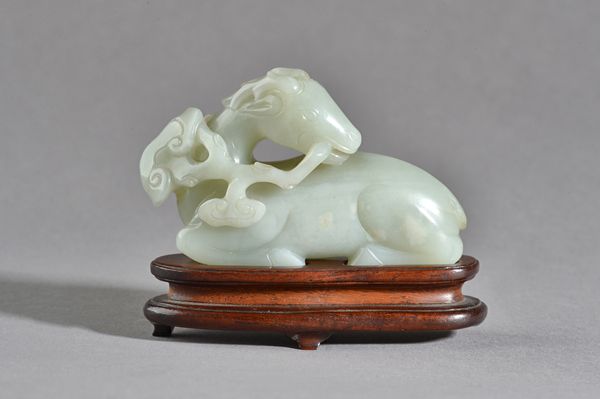 A Chinese celadon jade figure of a recumbent deer, 19th century, carved with head turned over its back and holding a branch of lingzhi in its mouth, t
