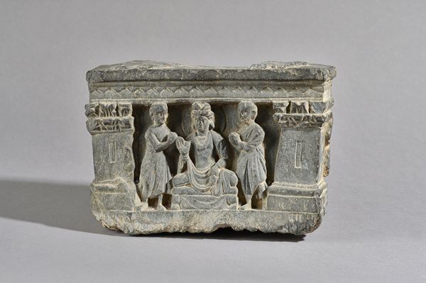 A Gandhara grey schist fragment from a statue base, 3rd/4th century, AD, depicting Buddha Maitreya flanked by devotees within a niche supported by Cor