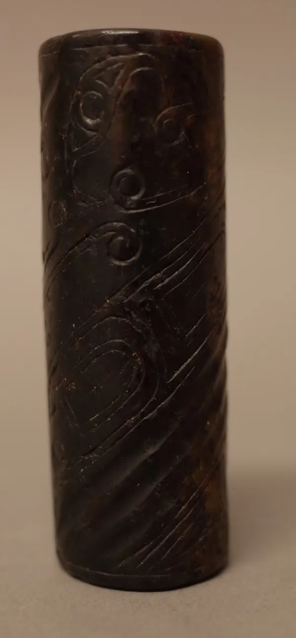 A Chinese archaic jade bead, of cylindrical form, carved with a spiralling band and incised with stylised scrolls, the stone of yellowish green and br