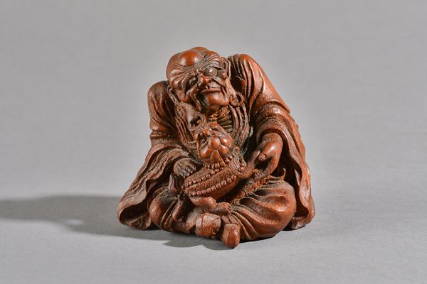 A Chinese bamboo figure of a luohan, amusingly carved seated with a playful pup tugging at a ring in his earlobe, 10cm. high. Illustrated