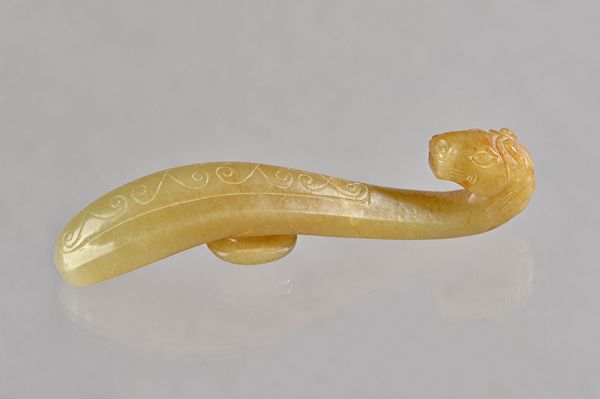 A Chinese jade belt hook, carved with a horse head hook, the curved shaft incised with scrolls, the stone of greyish brown tone, 9.5cm. length. Illust