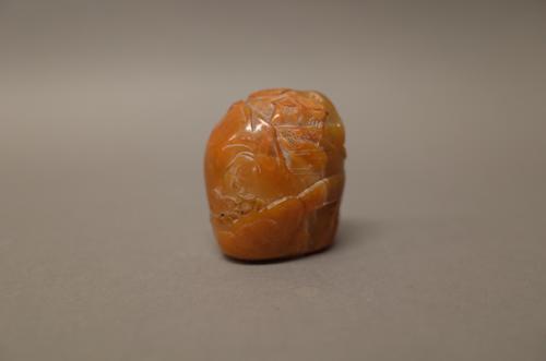 A Chinese brown soapstone boulder seal, probably 18th century, carved on one side with buildings, a fence and a bridge, the reverse carved with a figu