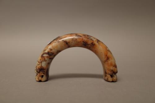 A Chinese jade arched pendant probably Yuan/Ming dynasty, carved at each end with a dragon mask, the stone of cream tone with reddish-brown and dark b