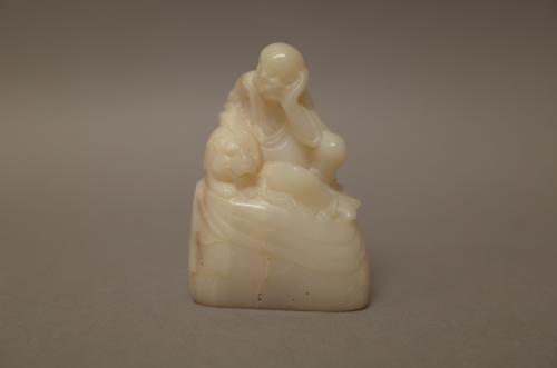 A Chinese white soapstone group, probably 19th century, carved as a luohan seated with one arm resting on a recumbent tiger at his side, incised chara