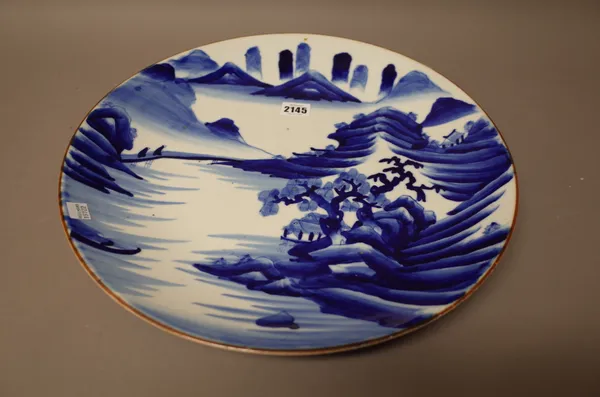 An Arita blue and white dish, Meiji period, painted with buildings and two figures crossing a bridge in an extensive mountainous landscape, 40cm. diam