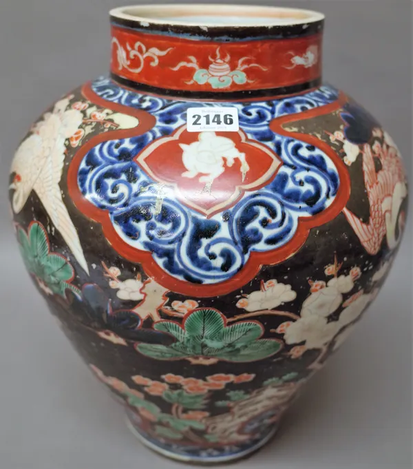 A Japanese porcelain ovoid vase, Edo period, painted in underglaze-blue with leafy scrolls framing a shaped black ground panel enamelled with storks a