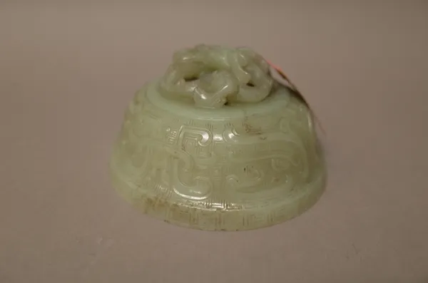 A Chinese celadon jade cover, 18th/19th, of domed form, carved with taotie masks between key pattern borders, the cover carved in high relief with a d