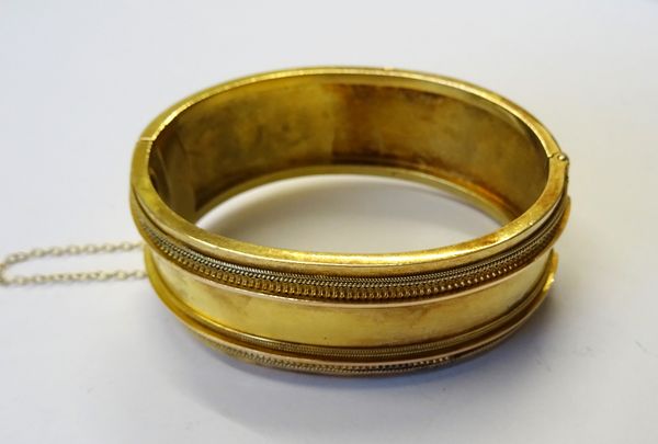 A Victorian gold oval hinged bangle, the front with applied decoration in the classical taste, on a snap clasp, detailed 15 C, fitted with a safety ch