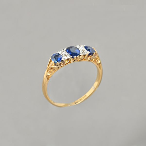 A gold and platinum, sapphire and diamond ring, mounted with three oval cut sapphires and with two pairs of cushion shaped diamonds, mounted at interv