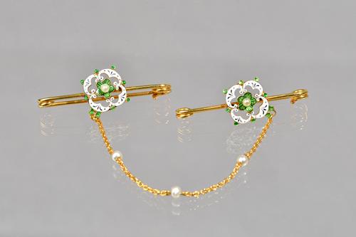A pair of gold, green, black and white enamelled and seed pearl set bar brooches, connected by a gold chain, spaced with three pearls at intervals, wi