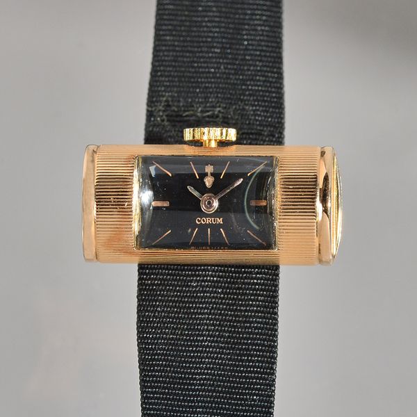 A Corum cylindrical cased lady's gold wristwatch, the signed rectangular black dial with gilt baton numerals, the cylindrical case with reeded decorat