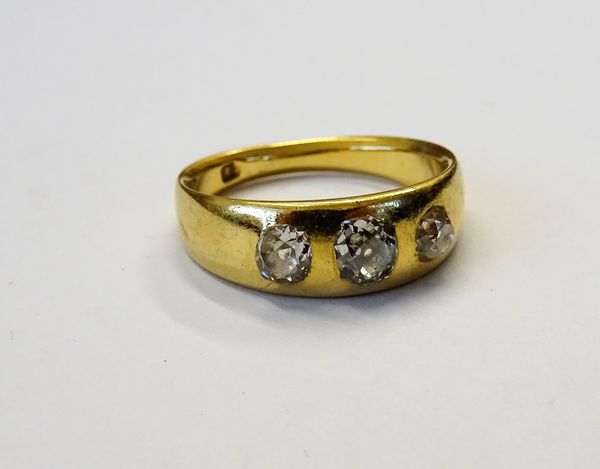 A gold and diamond set three stone ring, gypsy set with a row of cushion shaped diamonds, detailed 18, ring size J 1/2, gross weight 4.7 gms.