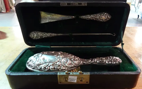 A late Victorian silver mounted three piece dressing set with embossed decoration, cased.