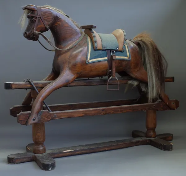 An early 20th century stained pine rocking horse on a wrought iron and stained pine swing frame base, 82cm high.