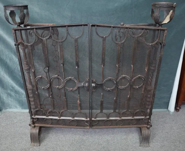 A 20th century blacksmith's made fire guard, with double hinged front and side screens and integral chimney cranes, mask finial terminals, 137cm wide