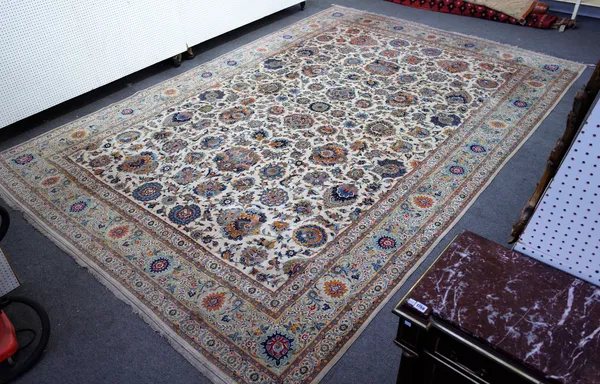 An Isfahan carpet, Persian, the ivory field with a small central roundel, with bold floral and palmette sprays; a grey palmette border, 546cm x 375cm.
