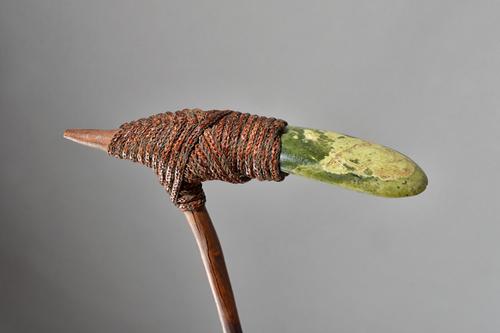 A New Guinea green hardstone adze, rattan bound to a naturalistic wooden haft, 53cm. Illustrated