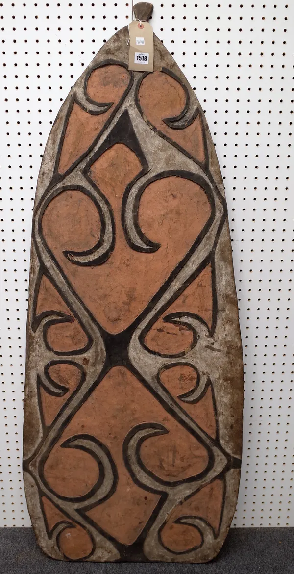 An Asmat wooden shield, West Papua, with relief carved geometric decoration, orange and white detail against a tapering ground, 140cm high.