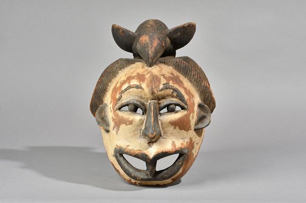 A West African Igbo mask, carved wood with bird head ornament and white pigment to face, 40cm and three further African tribal wooden masks, (4). Illu