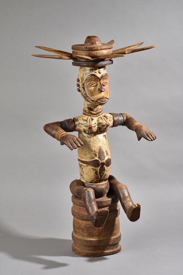 An African carved wooden tribal figure, white pigment decoration, modelled seated on a drum with spiked crown head ornament, 78cm high. Illustrated