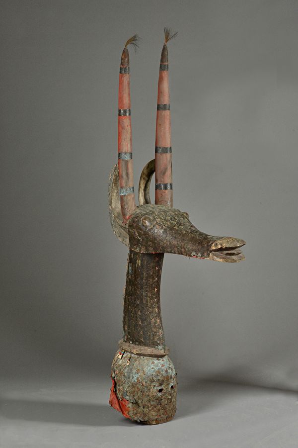 A West African zoomorphic hardwood helmet mask, decorated with copper, textile, cowrie shells and horse hair, 160cm high. Illustrated