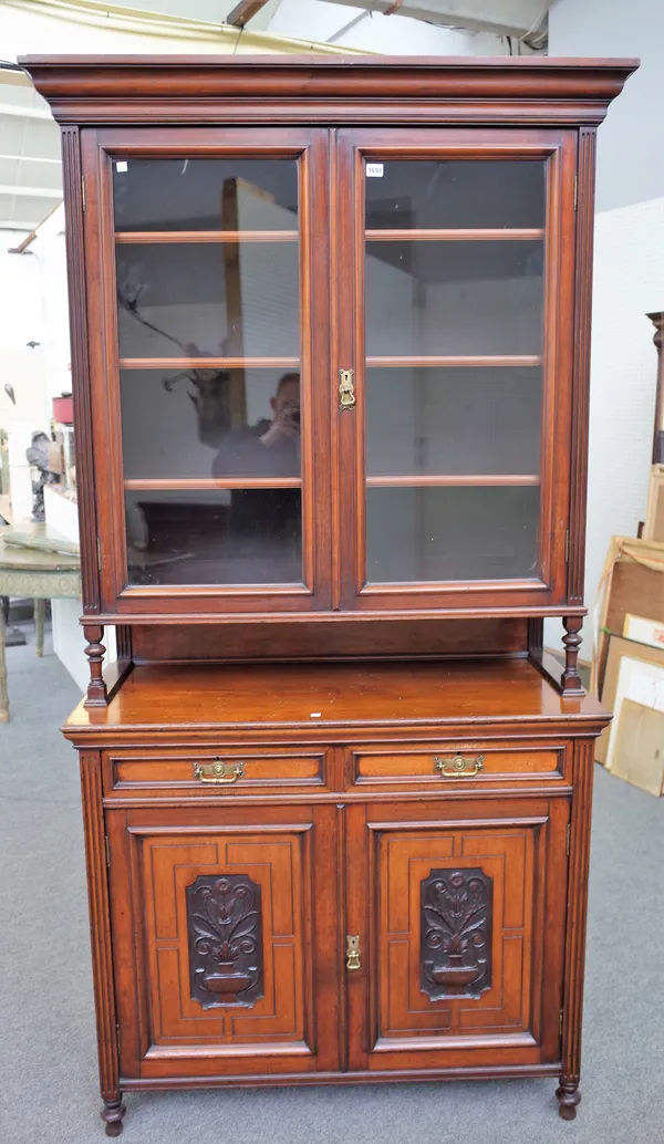 Maple & Co; a late Victorian walnut bookcase cabinet with pair of glazed doors over pair of drawers and cupboards with relief floral carved panels on