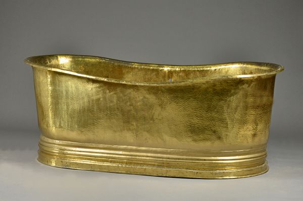 A 20th century beaten brass bath, with roll-over top, 183cm wide x 68cm high. Illustrated